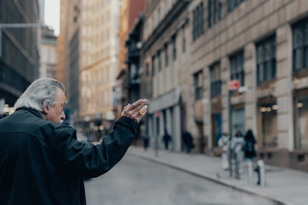 Elderly man waving on a city street.