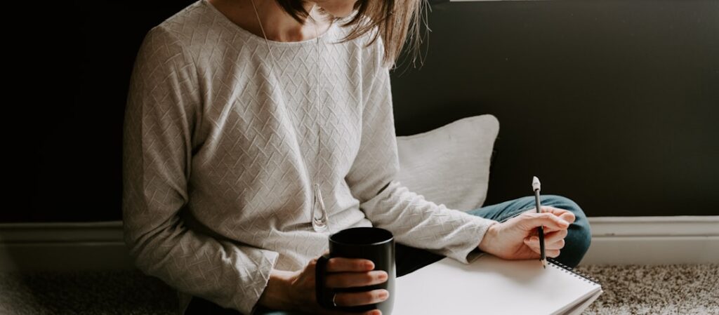 Woman writing in notebook with coffee cup