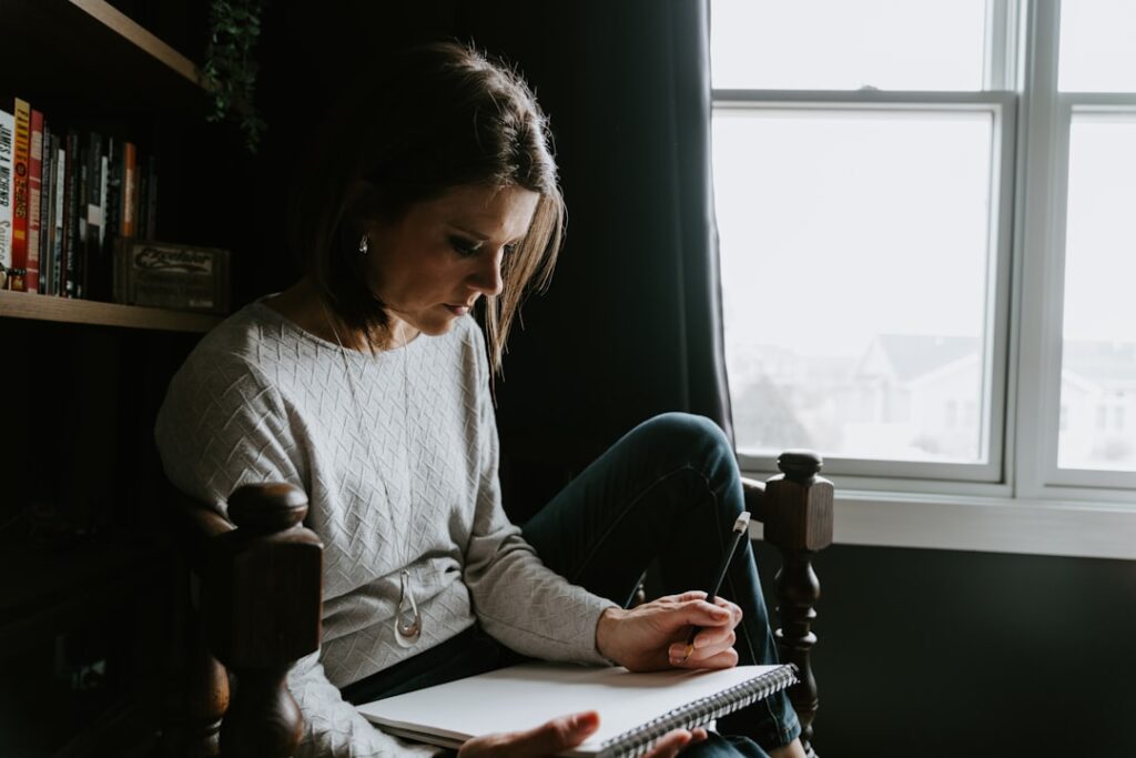 A woman sitting in a chair writing in a notebook.