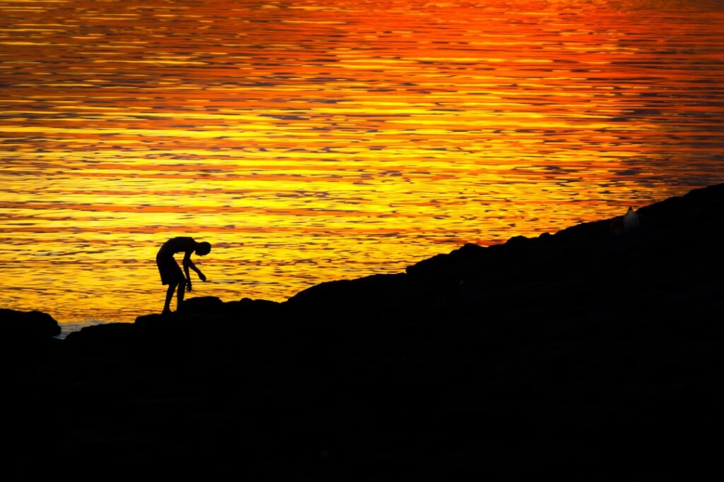 Silhouette of a person on a rocky shore at sunset.