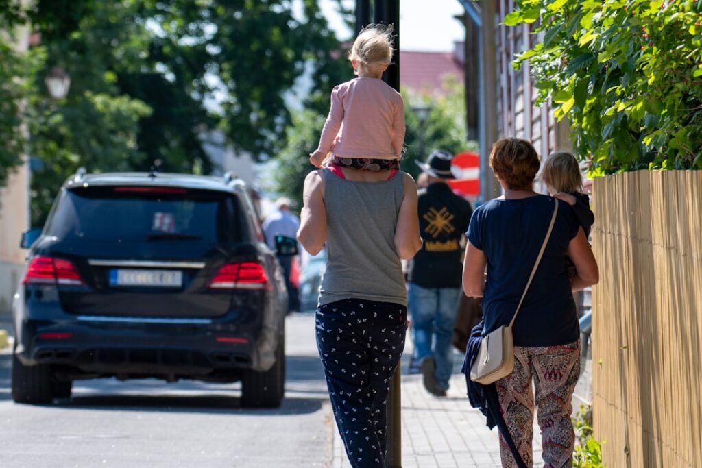 People walk on a sidewalk with a child on shoulders.