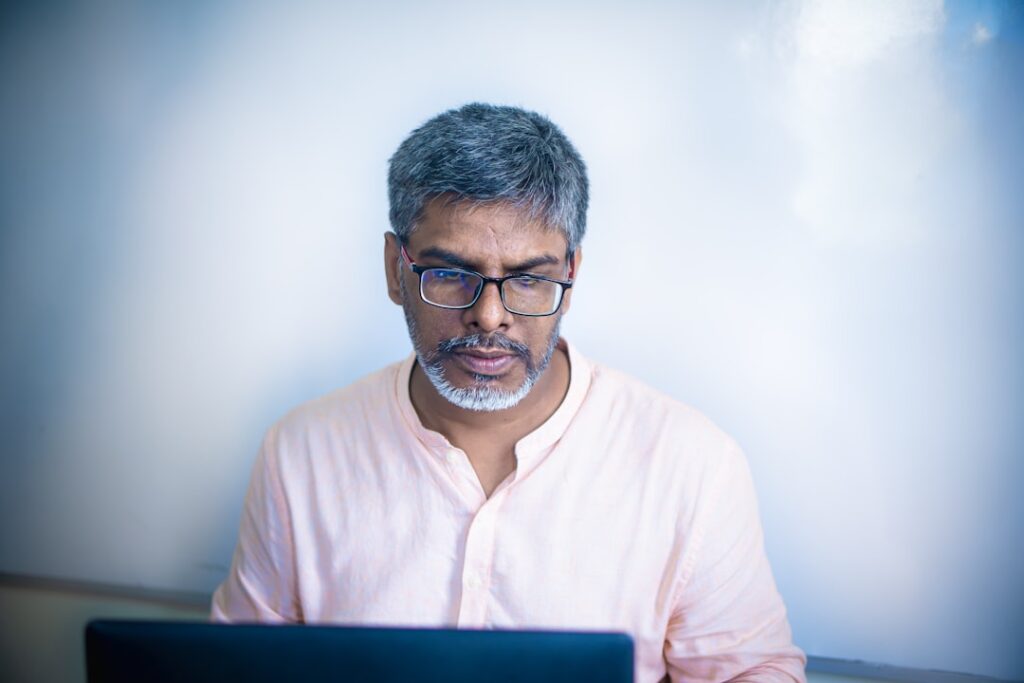 Man wearing glasses looking down at laptop.