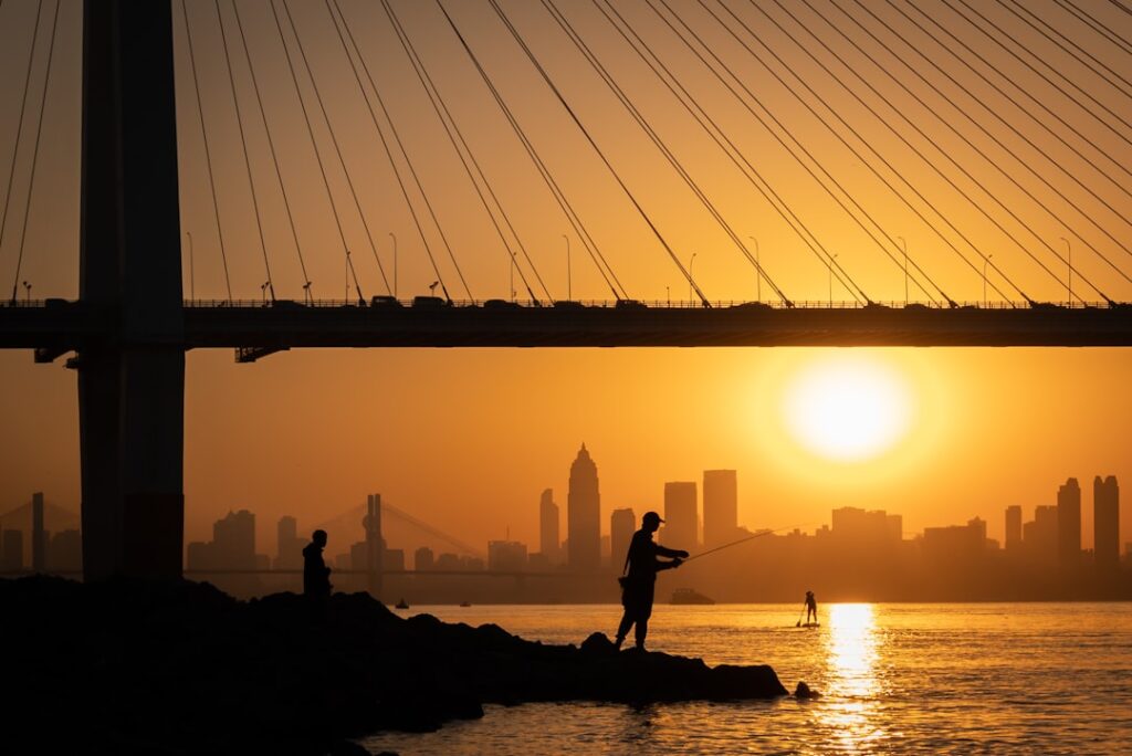 Fishermen enjoy the sunrise near a city skyline.