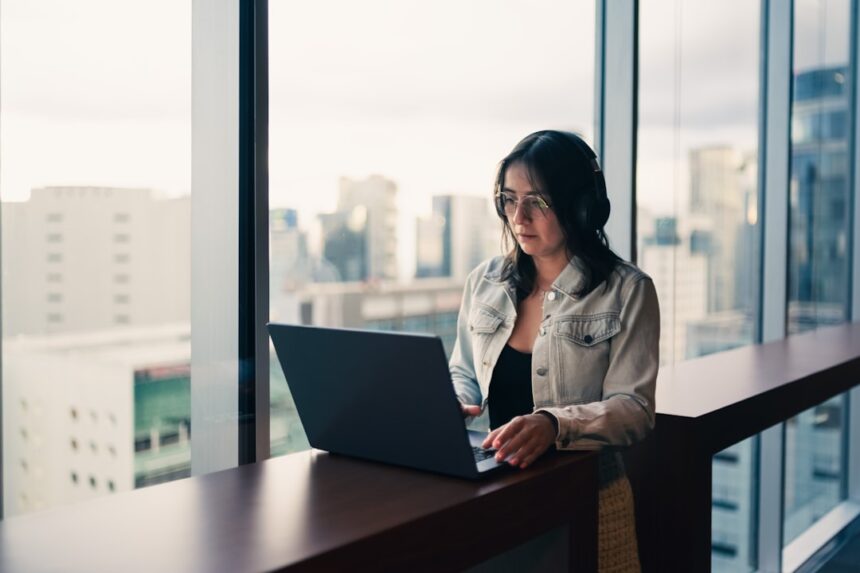 Woman wearing headphones working on a laptop by window