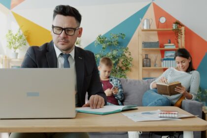 Man working on laptop while family relaxes in background