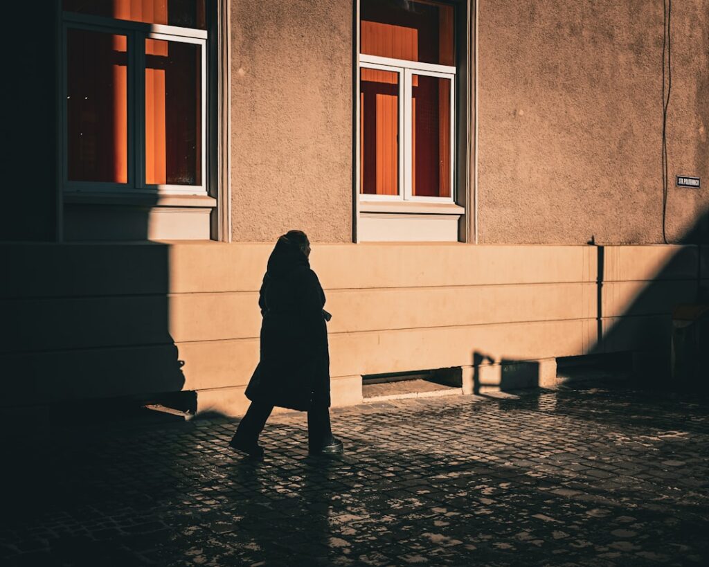 Silhouette of a person walking on a sunlit street.