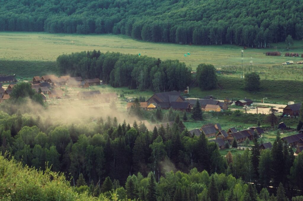 Dust cloud over a small village nestled in a forest.