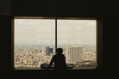 A silhouette views the city through a window.