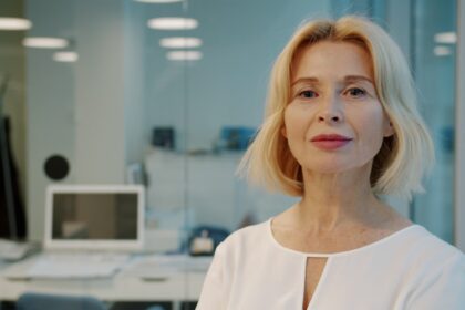 A blonde woman in a white blouse smiles
