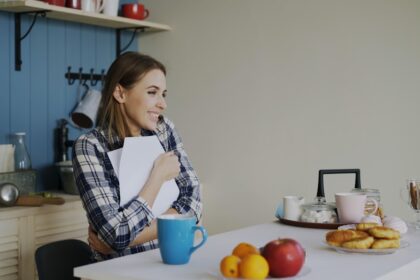 Woman holding book at kitchen table with snacks.