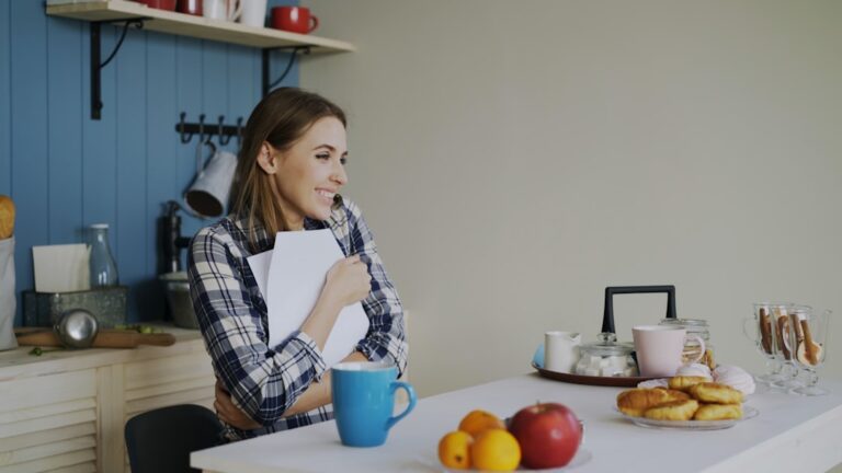 Woman holding book at kitchen table with snacks.
