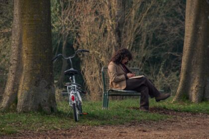 Person sitting on bench reading a book with bicycle.