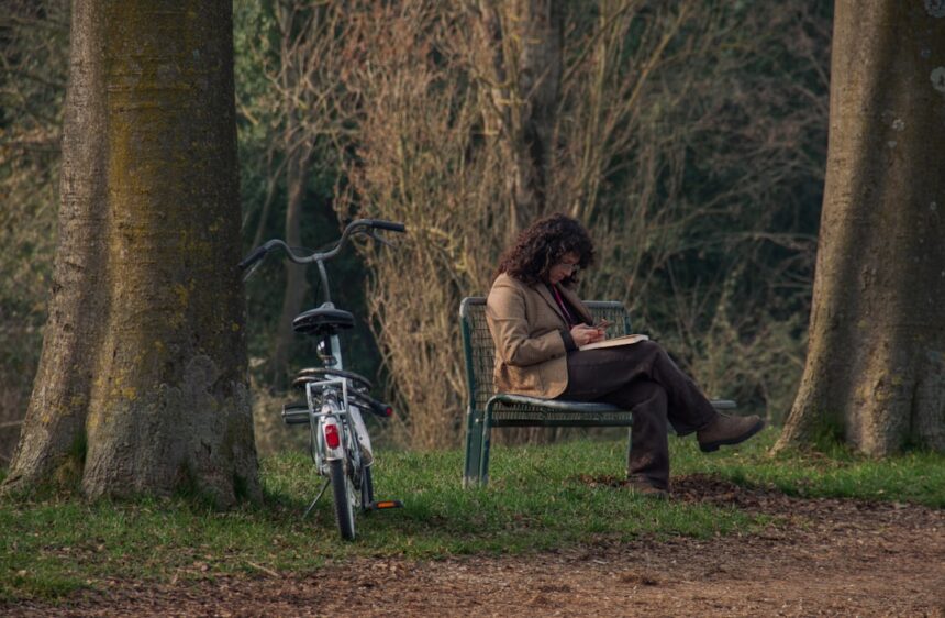 Person sitting on bench reading a book with bicycle.