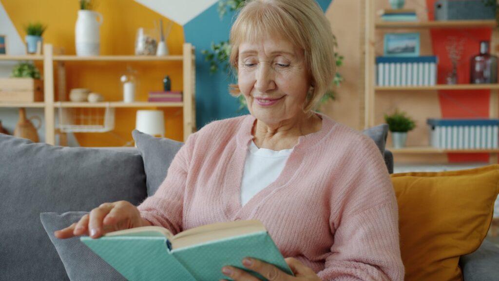 Elderly woman reading a book on a couch.