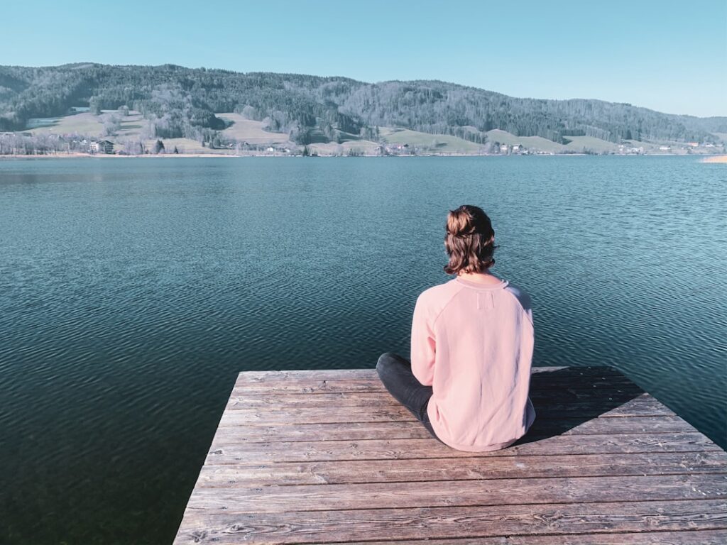 woman in white hoodie sitting on brown wooden dock during daytime