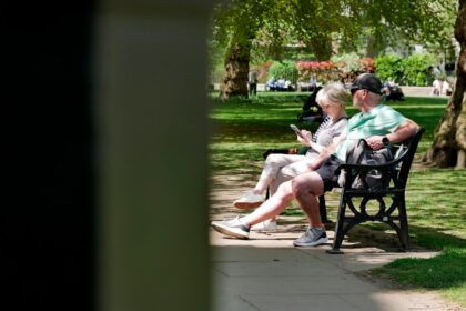 Couple sitting on a park bench looking at phones.