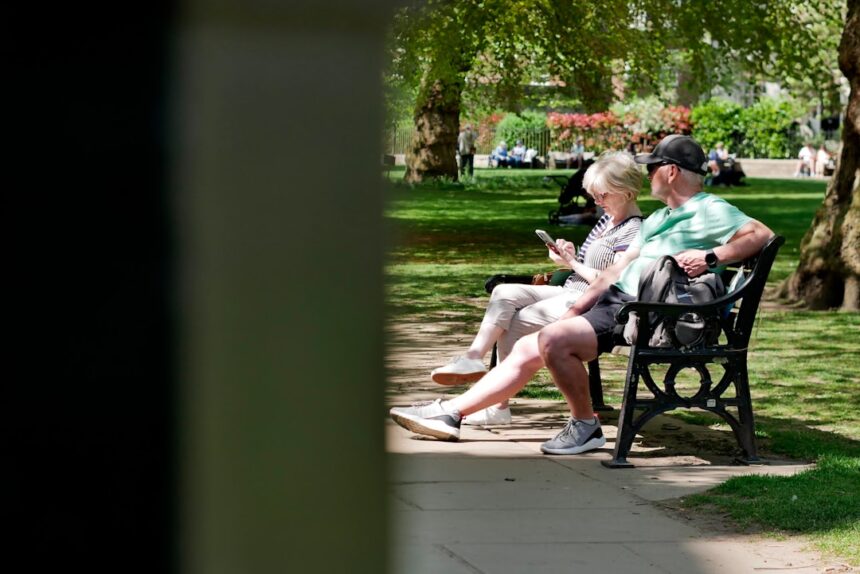 Couple sitting on a park bench looking at phones.
