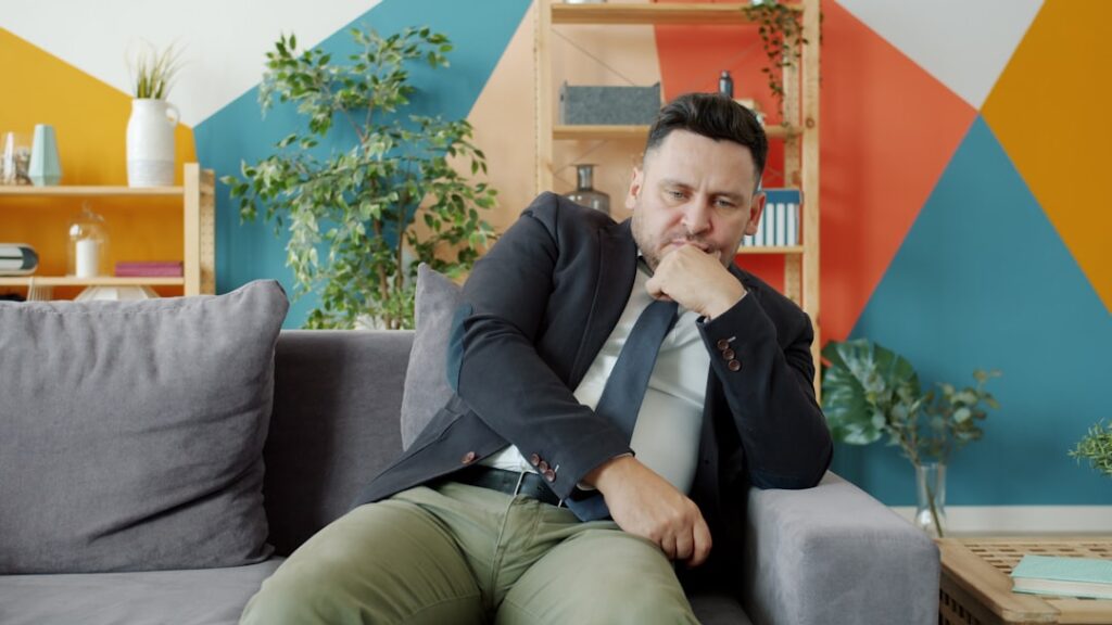 Man in suit sitting on couch looking thoughtful.