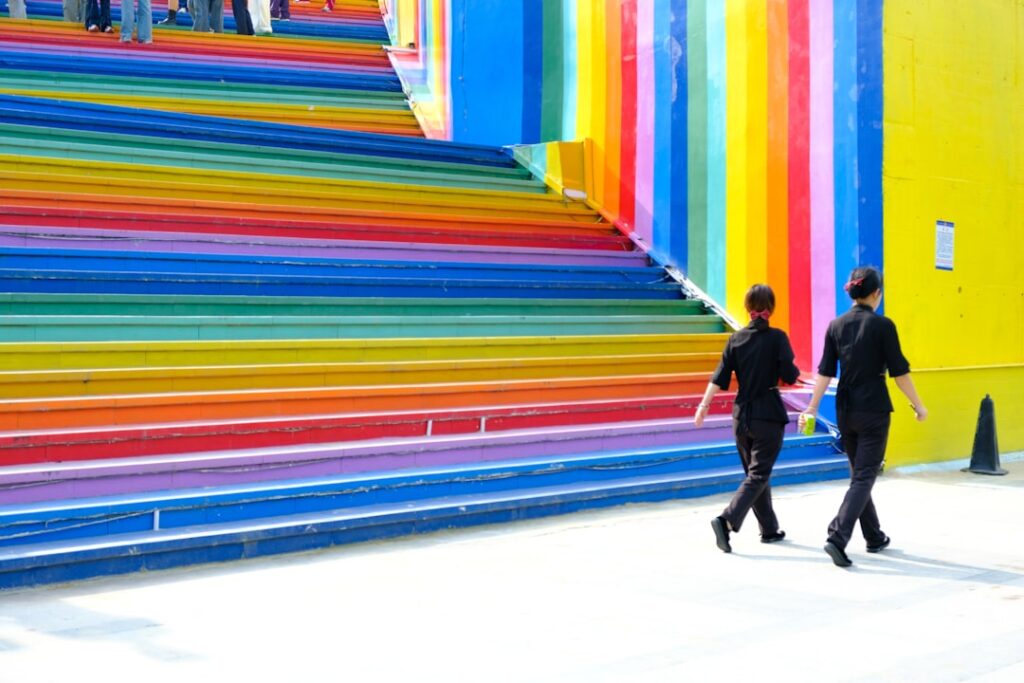 Two people walk up colorful rainbow stairs.