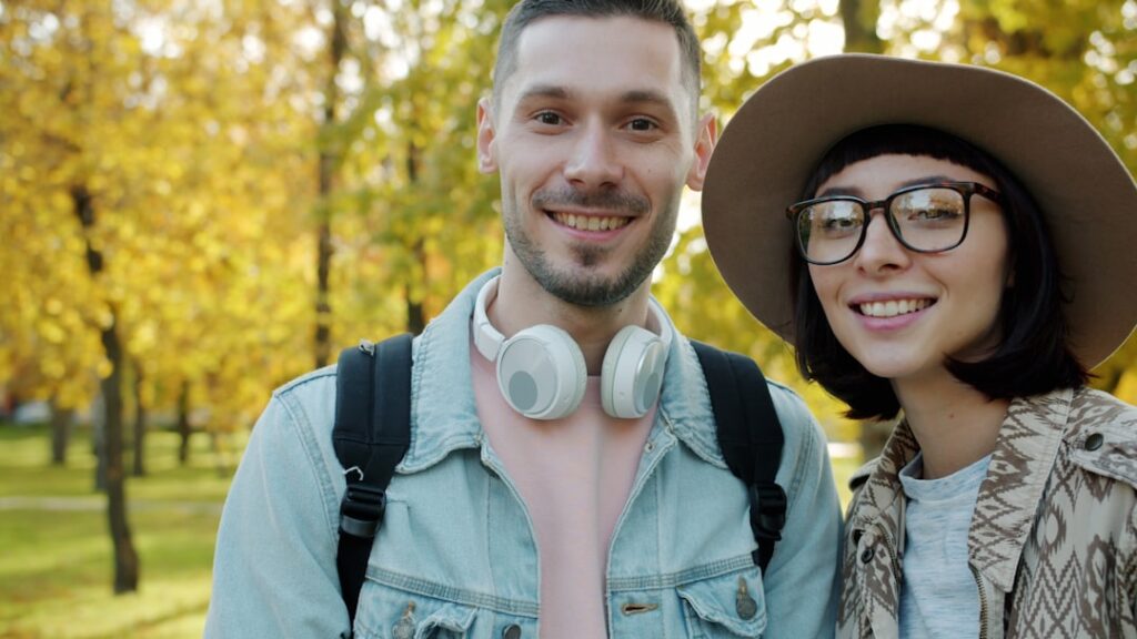 A smiling couple poses outdoors in autumn.