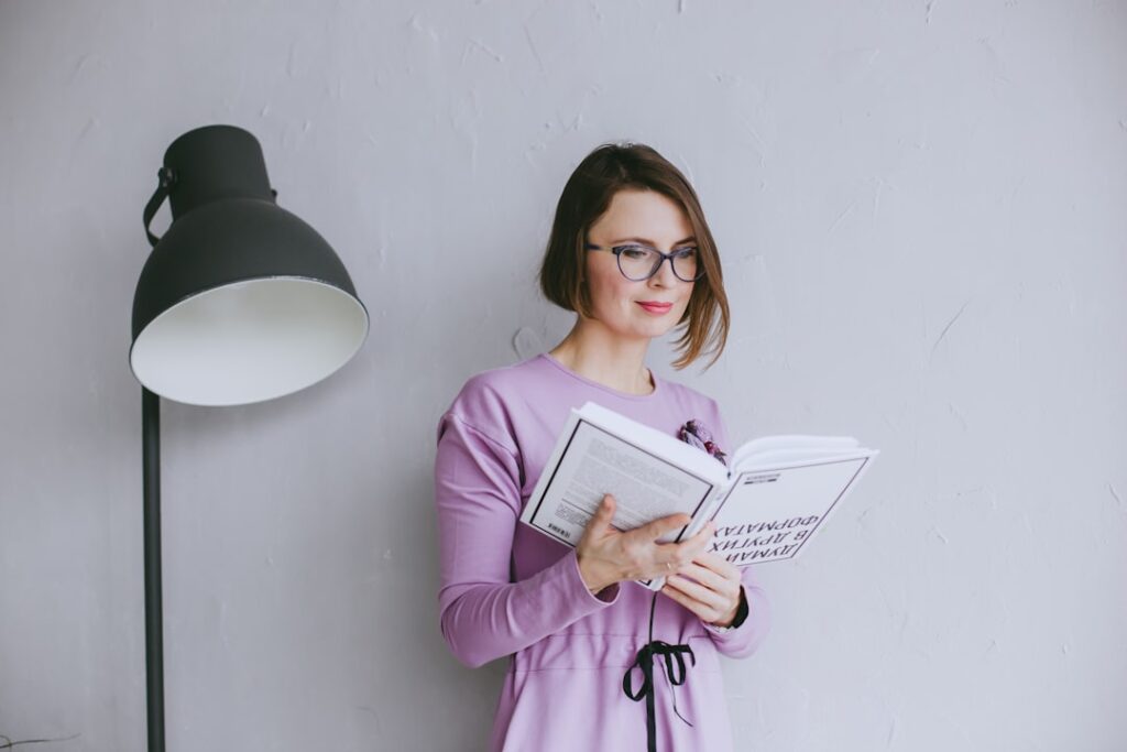 a woman standing next to a lamp reading a book