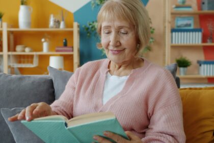 Elderly woman reading a book on a couch.