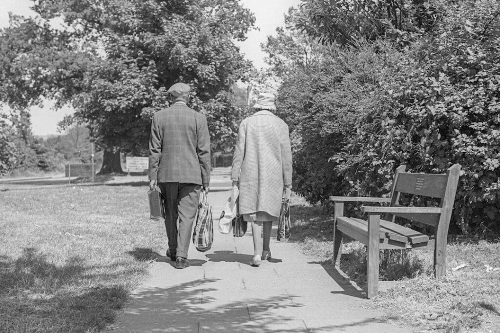 An elderly couple walks through a park.