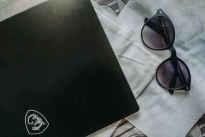 a laptop computer sitting on top of a bed next to a pair of sunglasses