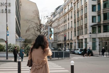 a woman in a trench coat is crossing the street