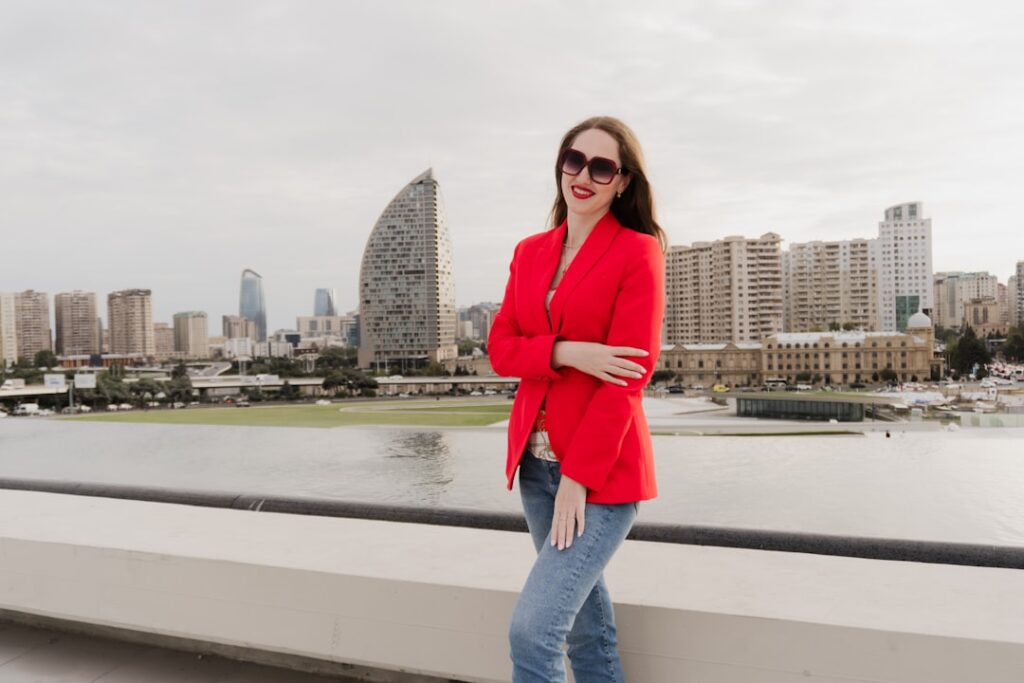 Woman in red blazer and jeans with city skyline.