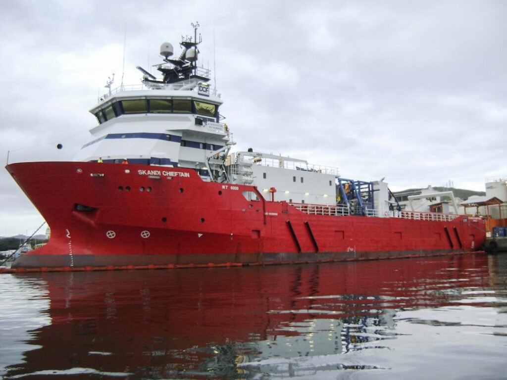 A large red offshore supply vessel docked at port.