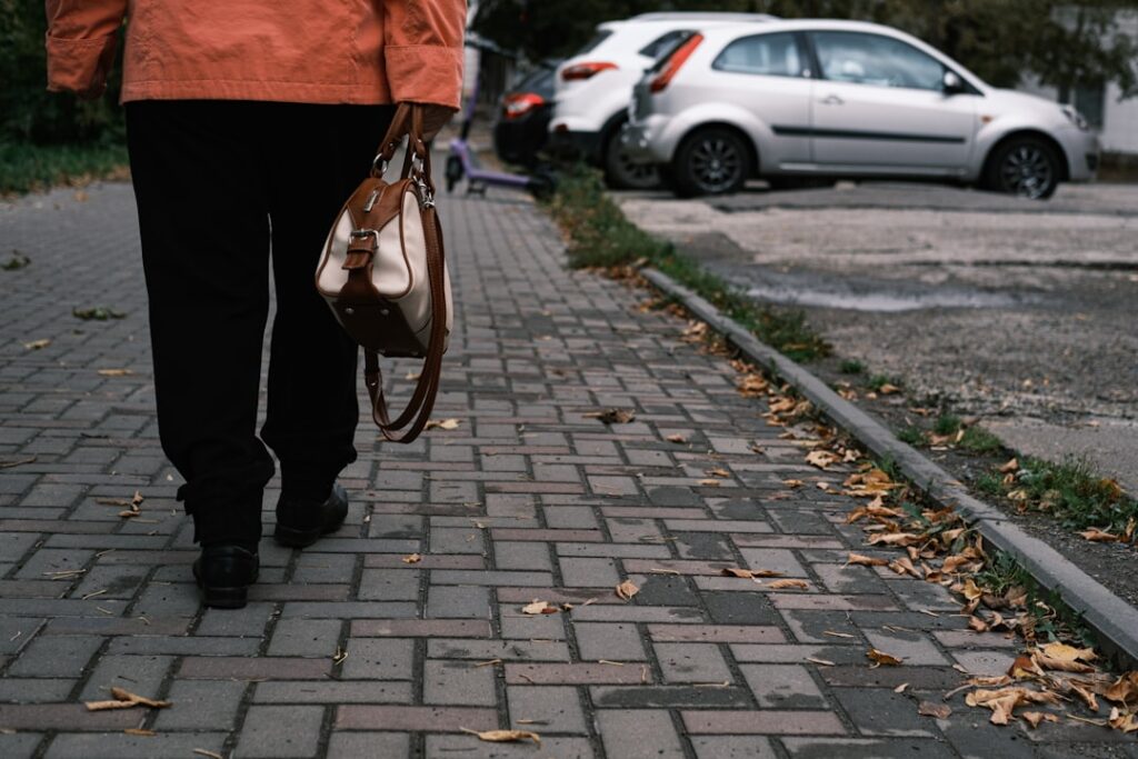 Person walking on a brick path with cars nearby.