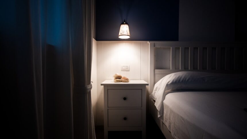 A bedside lamp illuminates a nightstand next to a bed.