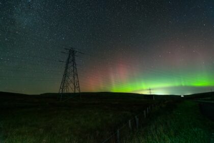 a green and red aurora over a field with power lines